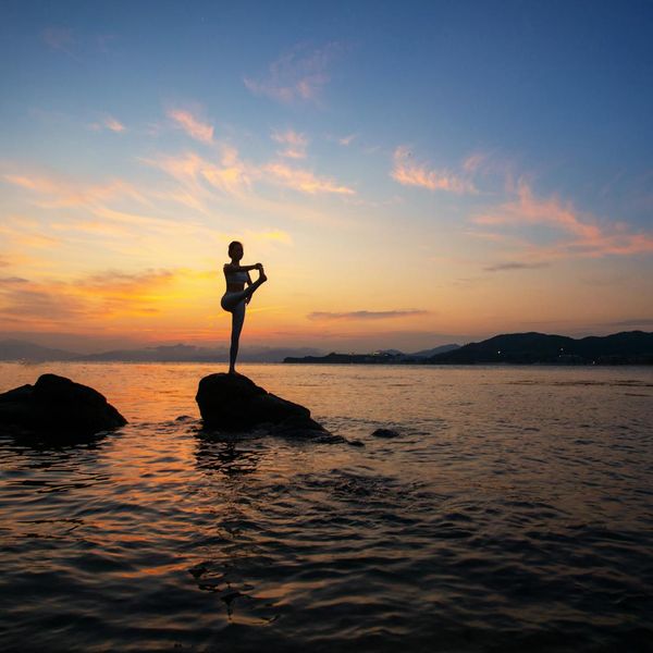 Silhouette of a person in a yoga pose against a sunrise.